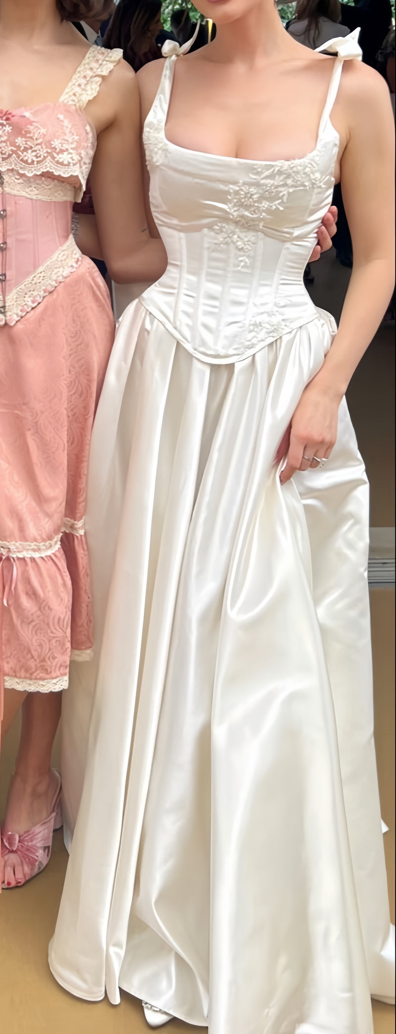 Woman wearing a white lace dress standing next to a pink dress.
